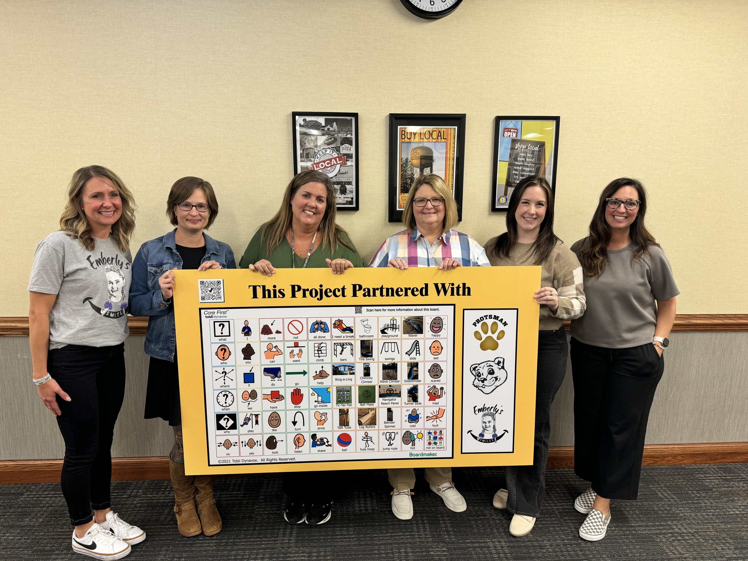 Staff from Bibich and Protsman display the new communication board from Emberly's Smiles, which will be installed on the Protsman playground. Boards will also be installed at Bibich, Homan, and Watson.